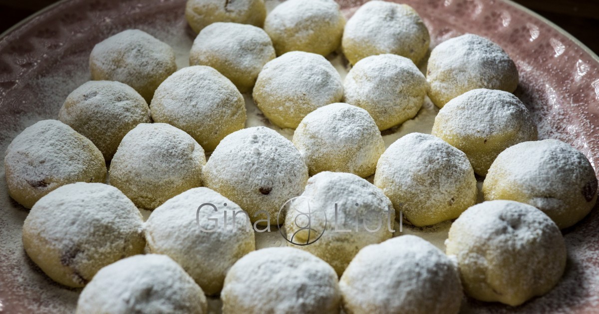 Two dozen Kourabiedes (shortbread balls) on a plate, sprinkled with powdered sugar